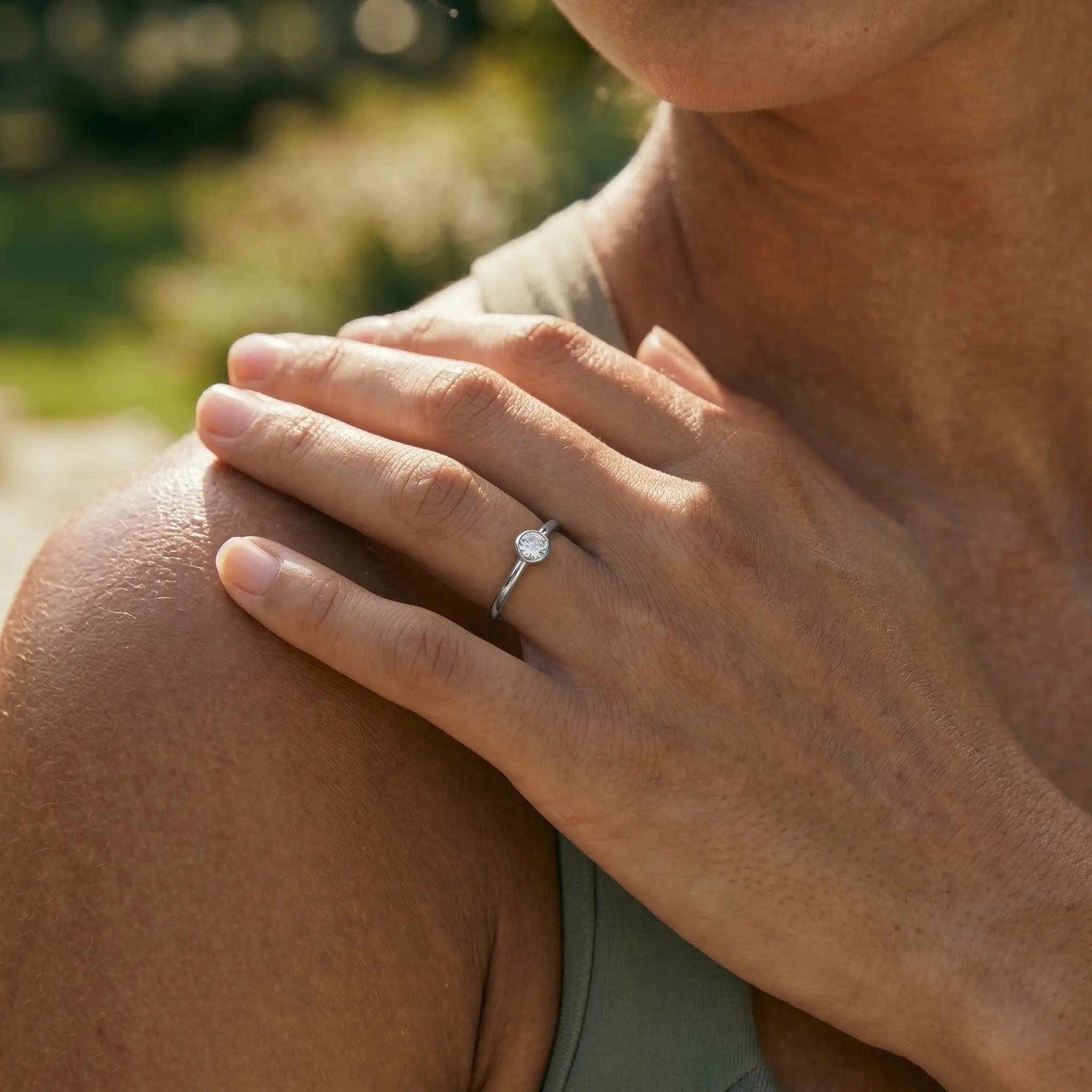 Close-up of a hand with a silver ring on a woman's shoulder.