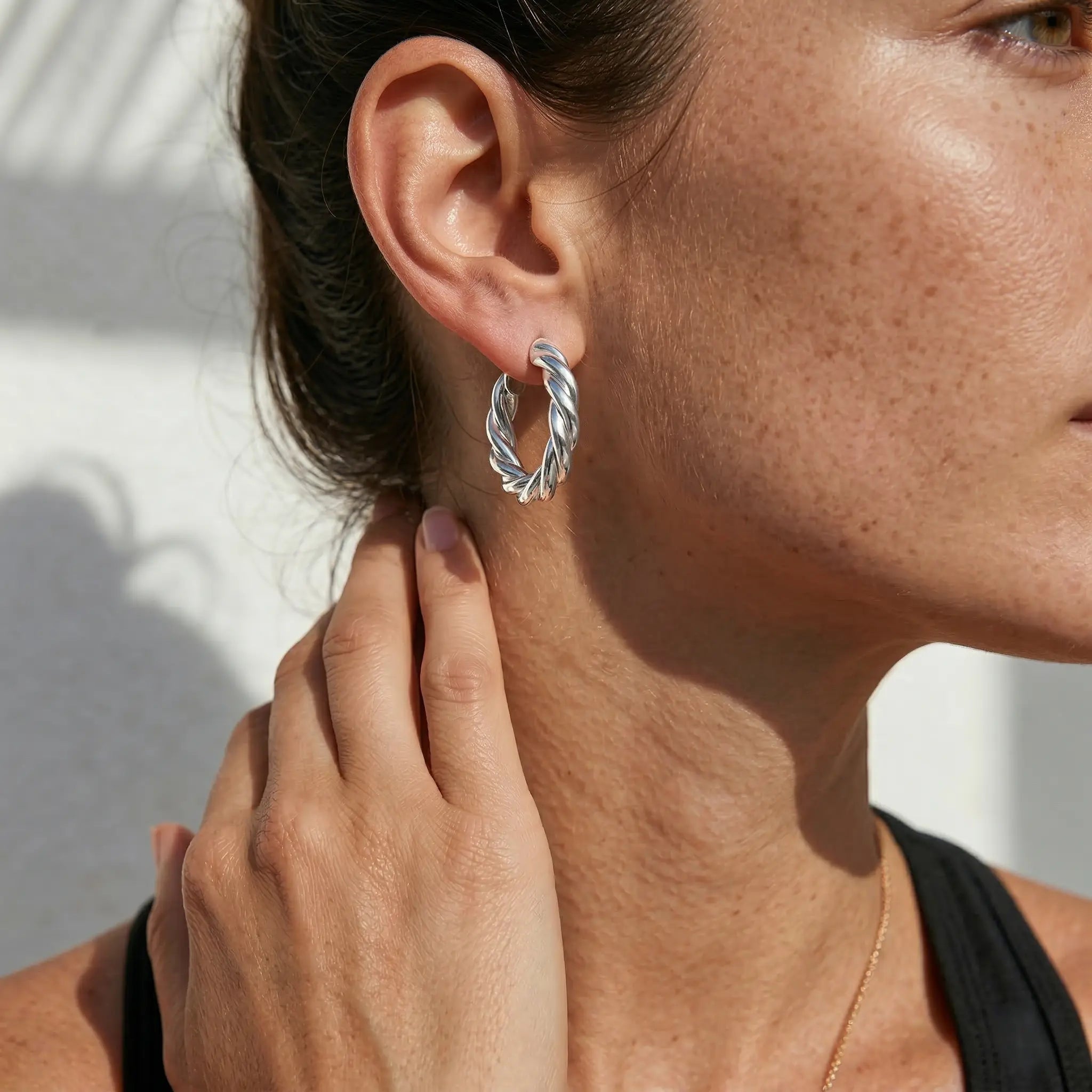 Close-up of a woman wearing silver plated hoop earring with a neutral background.