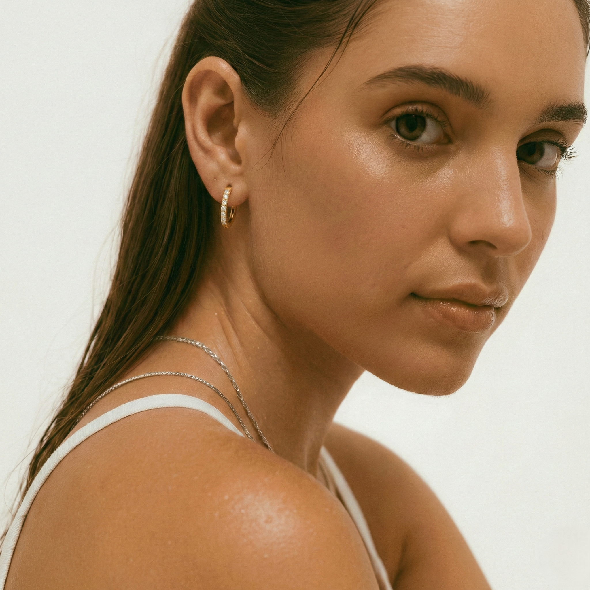 Close-up of a woman wearing gold hoop earrings against a neutral background