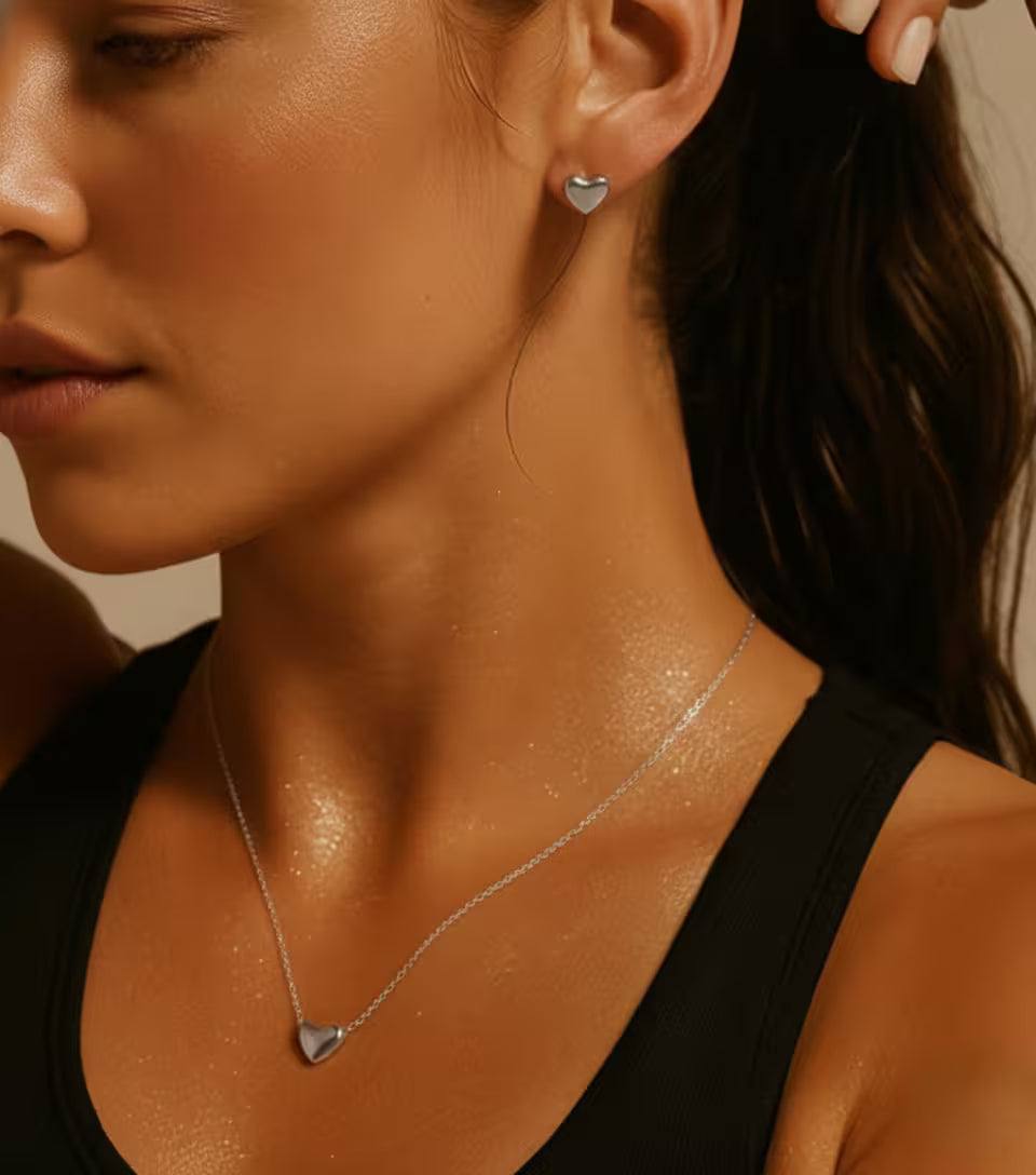 Close-up of a woman wearing a silver heart-shaped necklace and matching stud earrings.