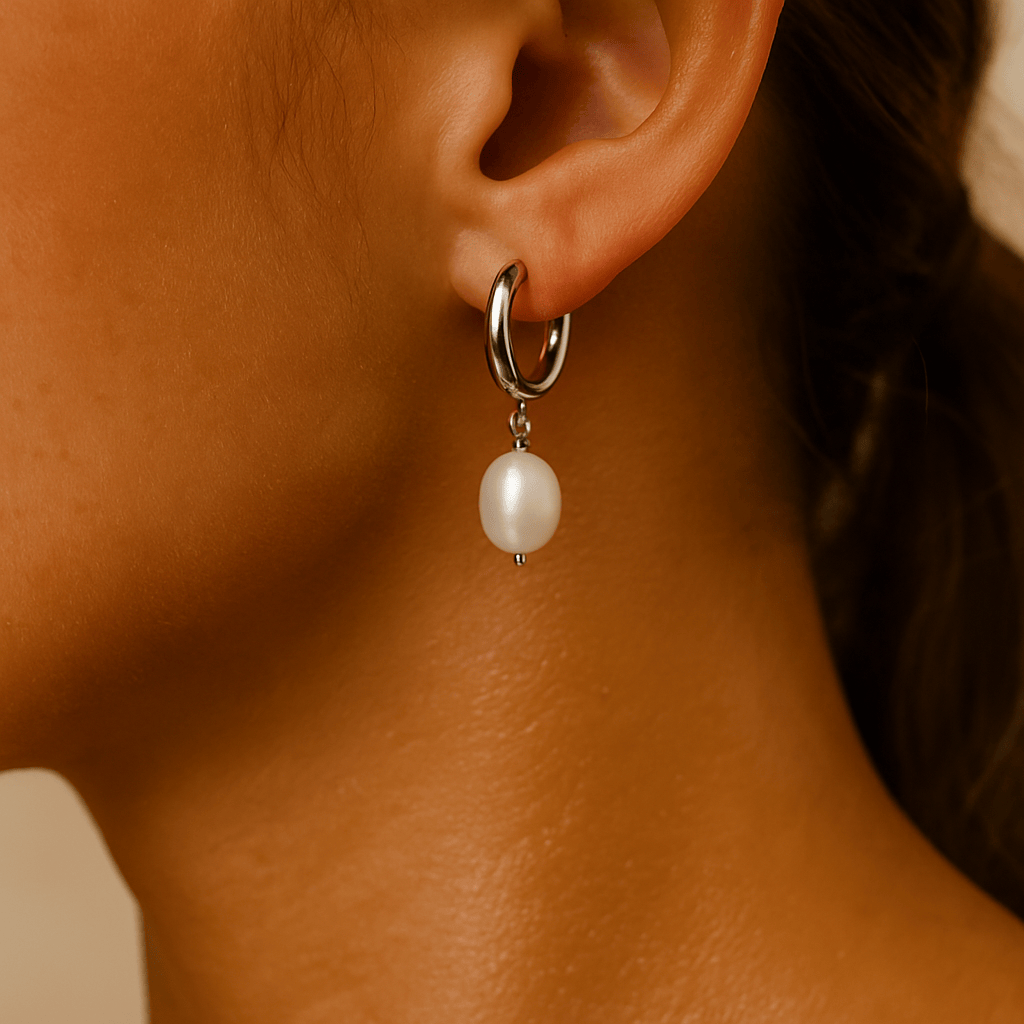 Close-up of an ear wearing a silver hoop earring with a pearl pendant.
